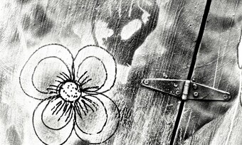 A black and white image of a flower and a raised fist drawn on a portion of a wooden door with a hinge.