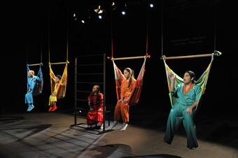 A group of performers hang in small hammocks onstage.