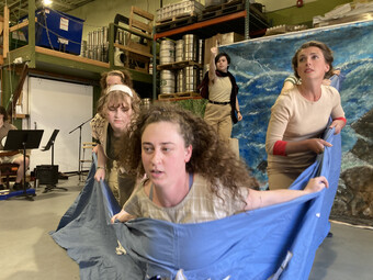 Three actors rehearse a scene with large pieces of blue fabric.