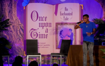 student with a mic standing on stage in front of an oversized book open to a page that reads once upon a time.