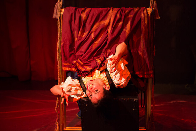 An actor in period costume hangs upside down in a frame on stage.