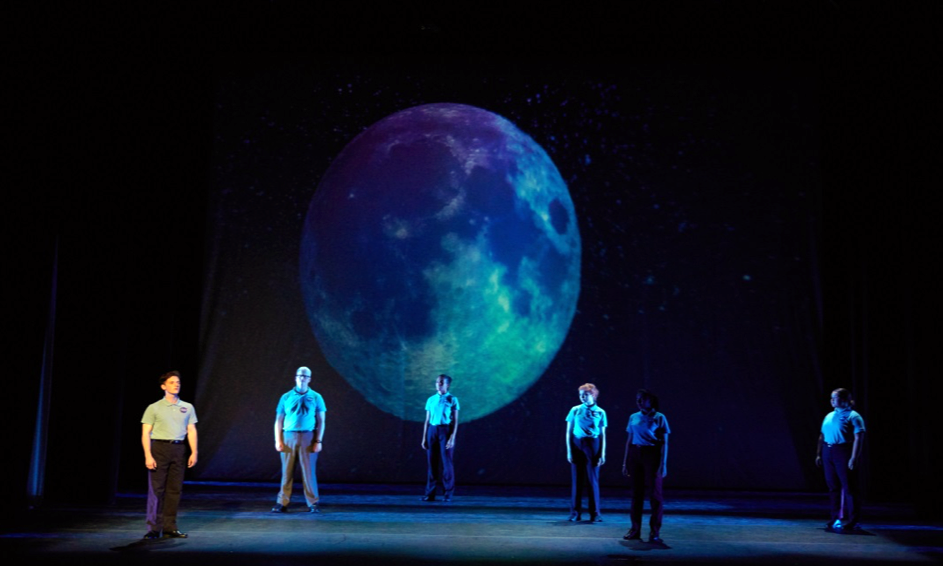 six actors onstage under a projection of the full moon