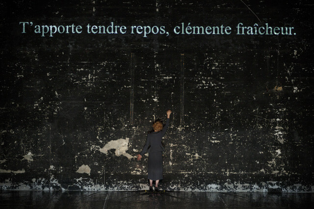 an actress onstage with text in french projected above her