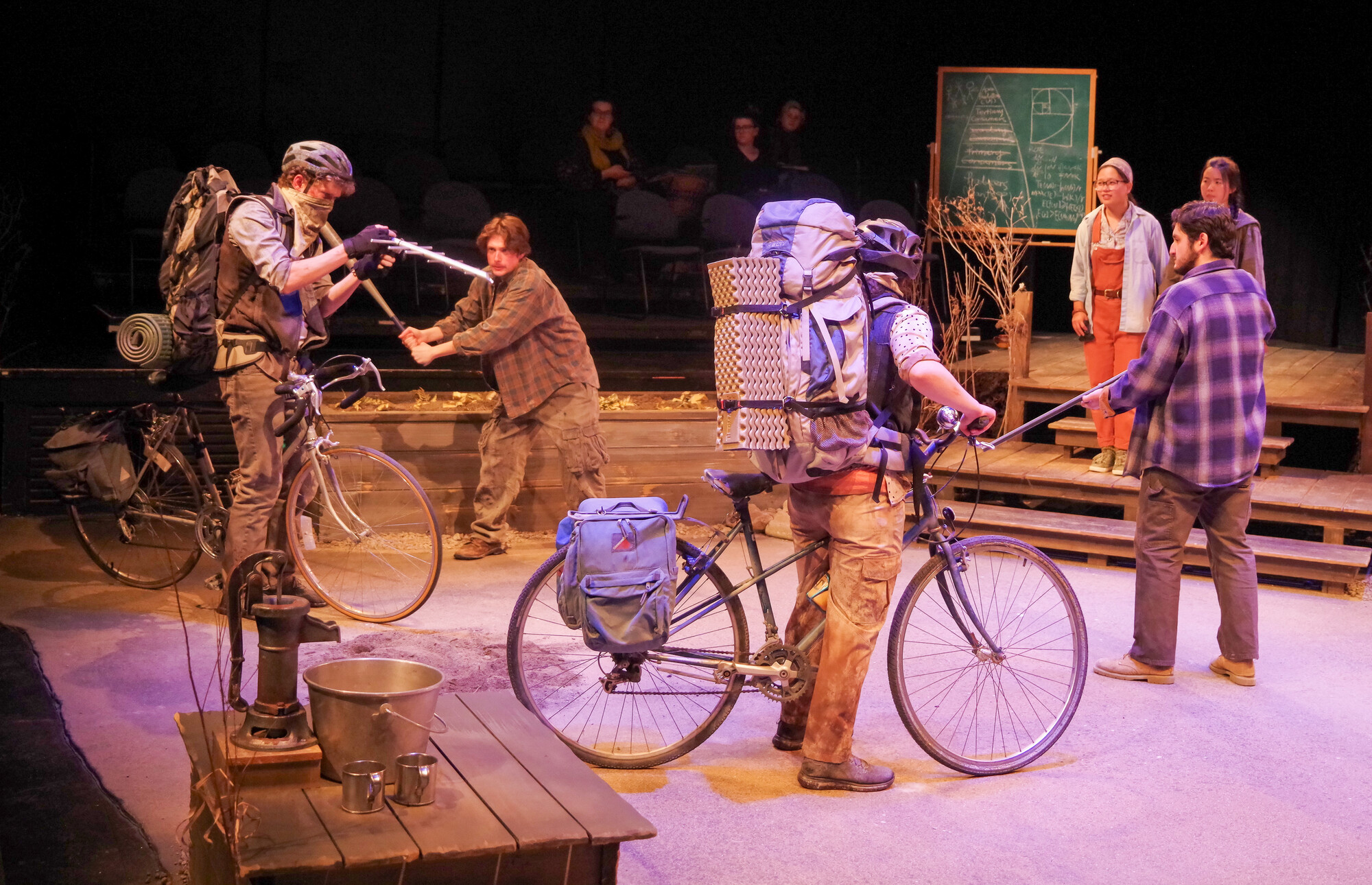 Six people on stage, one on a bike, talking excitedly amongst each other.