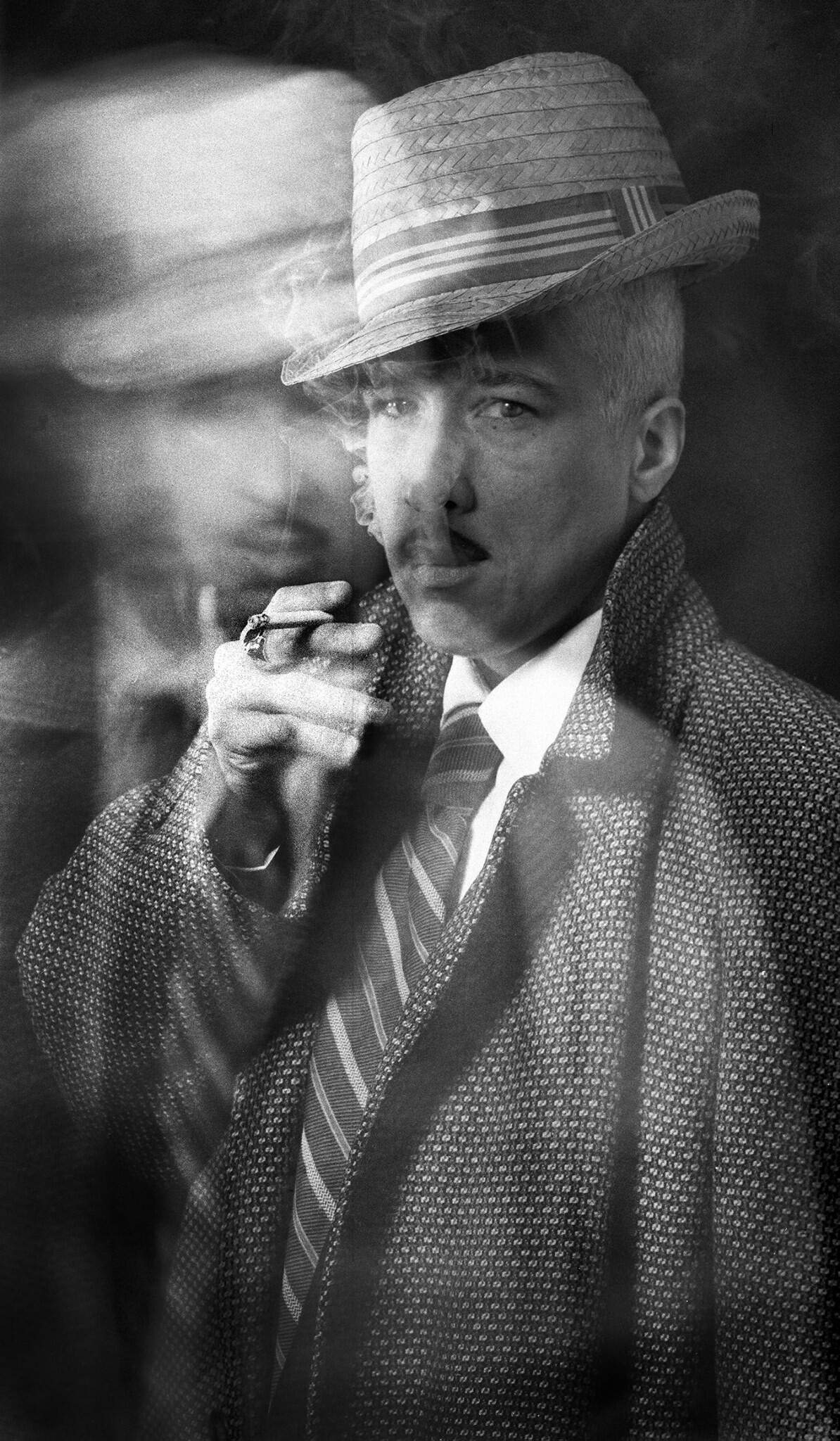 A blurred black and white portrait of a man in a suit smoking a pipe.