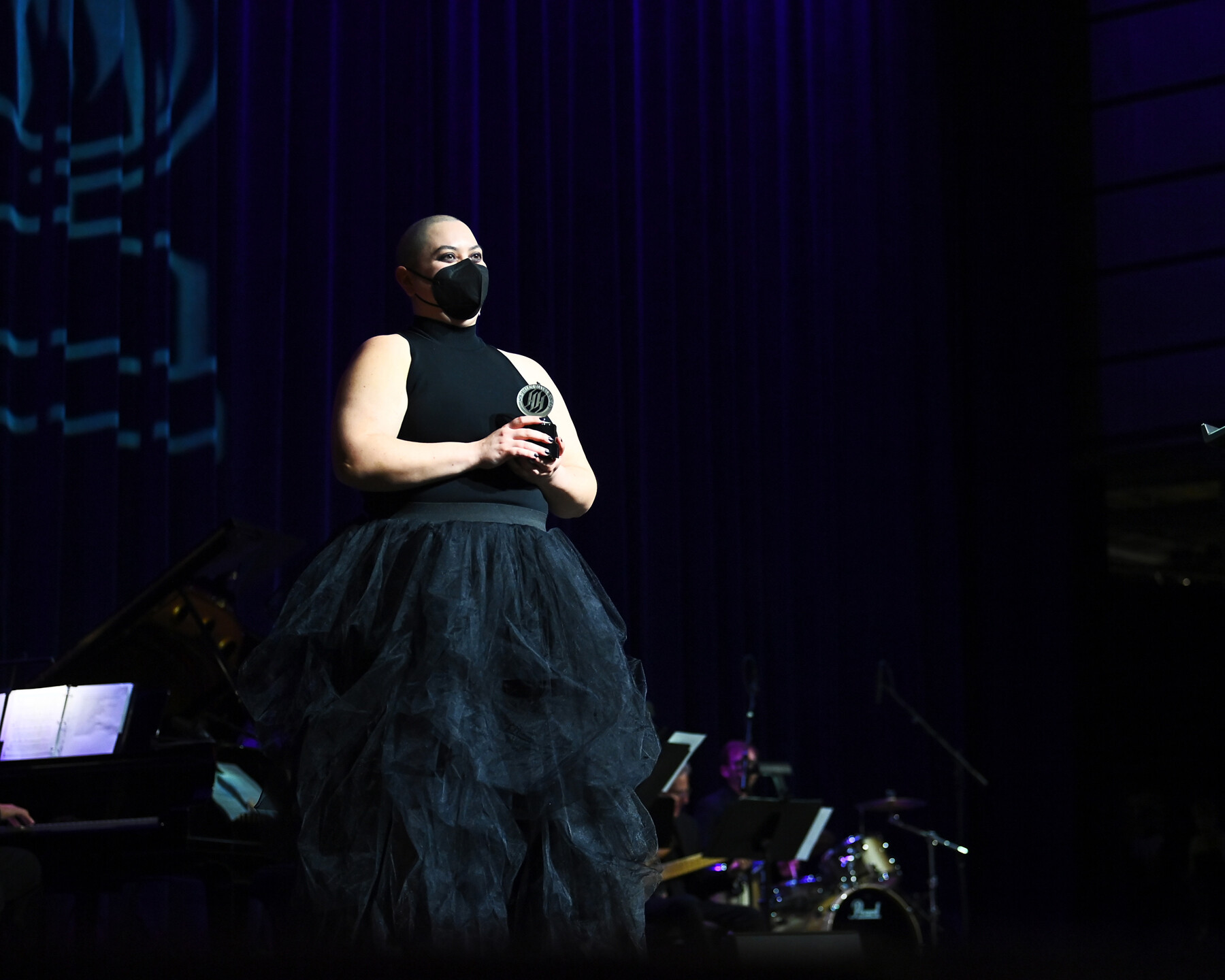 A person in a black mask presents an award onstage.