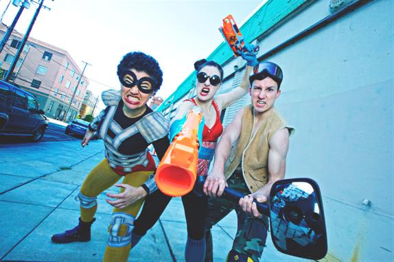 Three people in amateur superhero costumes posing on a sidewalk