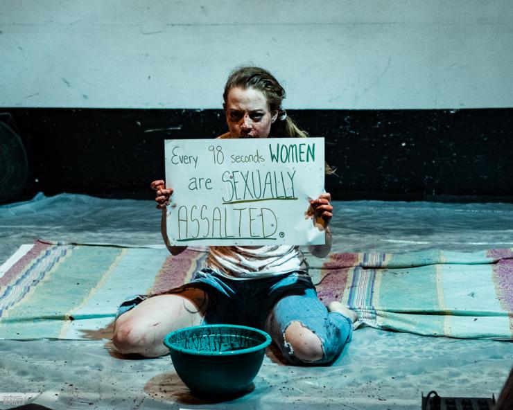 an actor kneels on the ground with a sign that reads: Every 10 seconds Women are sexually assaulted