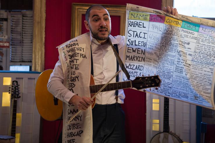 Performer with a guitar and holding a poster