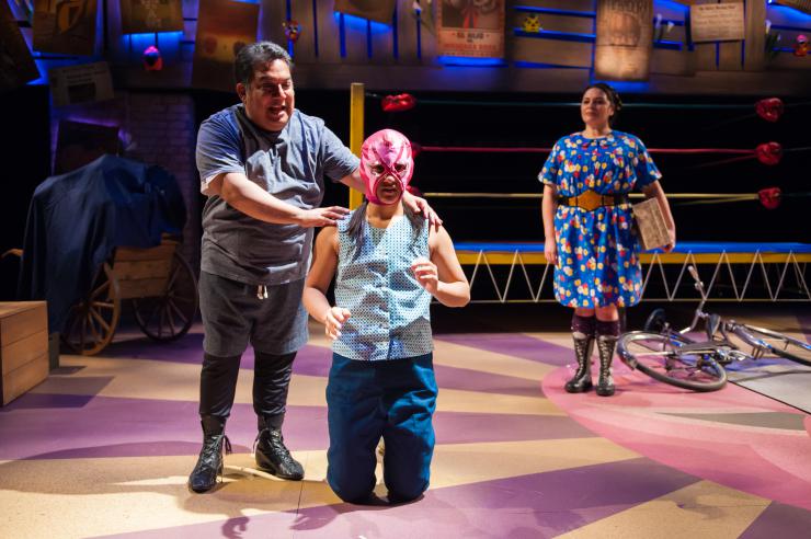 Three actors on stage, on wearing a luchador mask