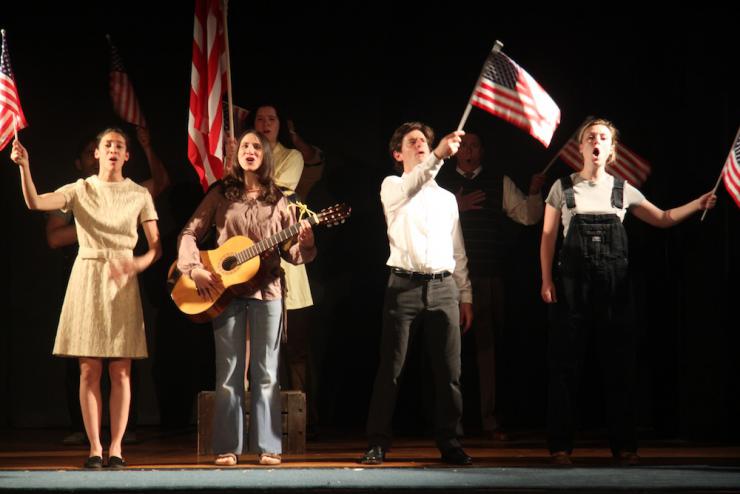 Four actors sing on stage and wave U.S. flags.