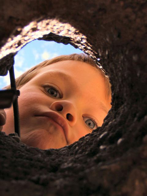 child peering down a hole in a playground