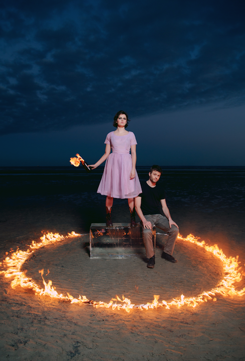 Two performers in a circle of fire, one stands on a block of ice and holds a molotov cocktail