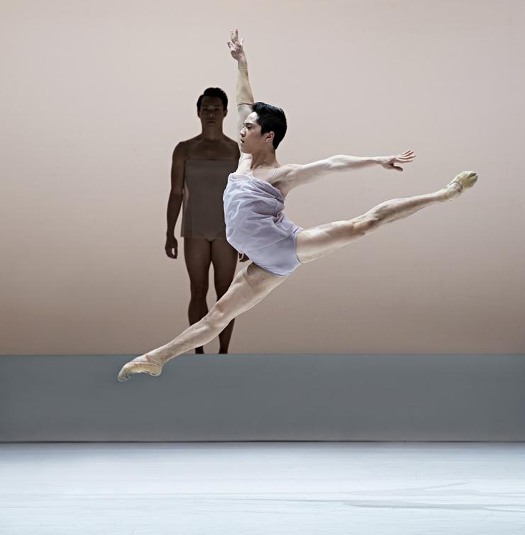 A dancer leaps while another watches on-stage. 
