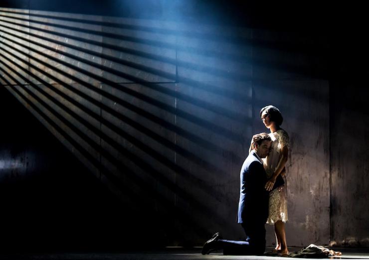 two performers embrace on a dimly lit stage