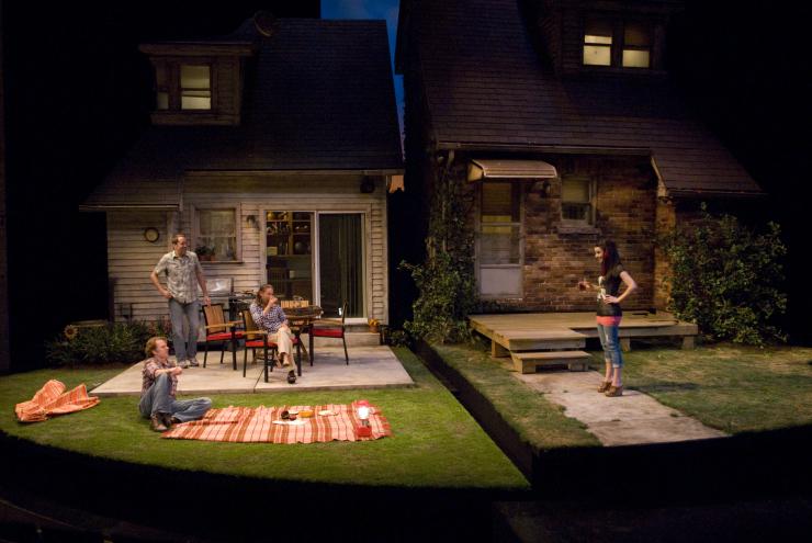 Four actors onstage in front of a suburban-style house.