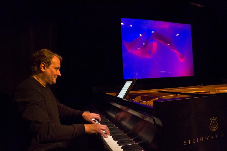 person playing the piano with a colorful puppet on a screen behind him
