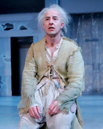 An actor onstage in ragged clothes and white hair.
