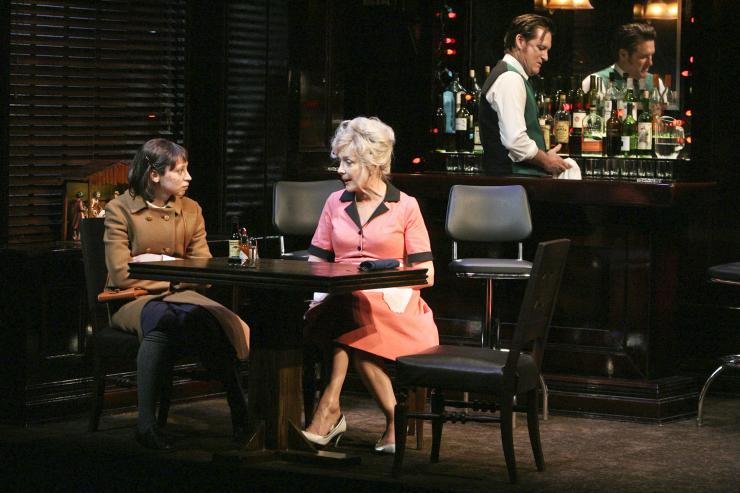 Two actors sit at a table in a bar.