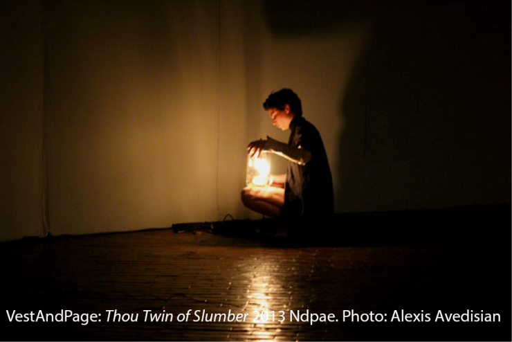An performer sits on the floor and holds a lantern.