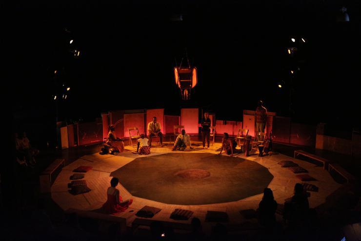 Actors sitting in various positions on a round stage.