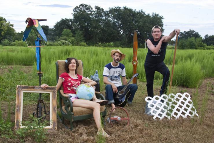 Three actors pose with furniture and props in a field