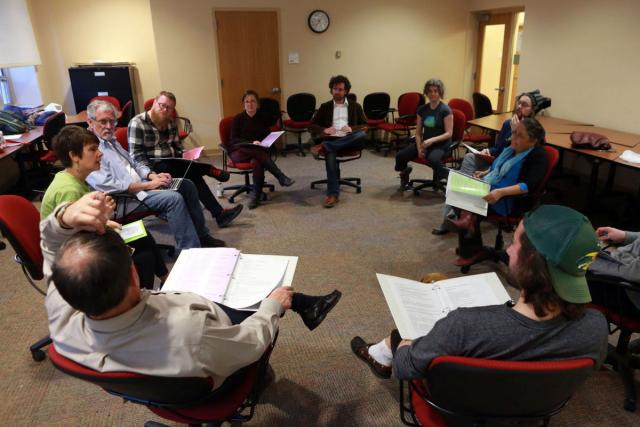 The cast sits in circle with scripts. 