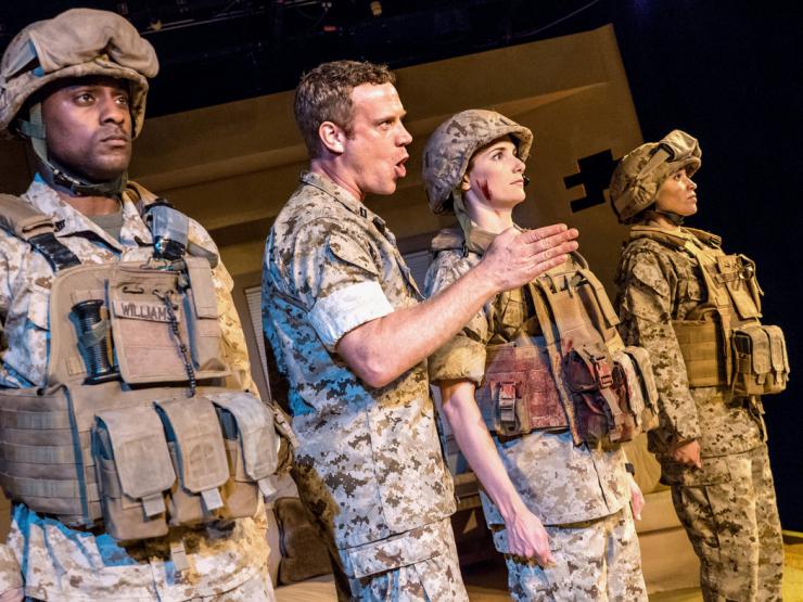 Four actors playing soldiers stand on stage. 