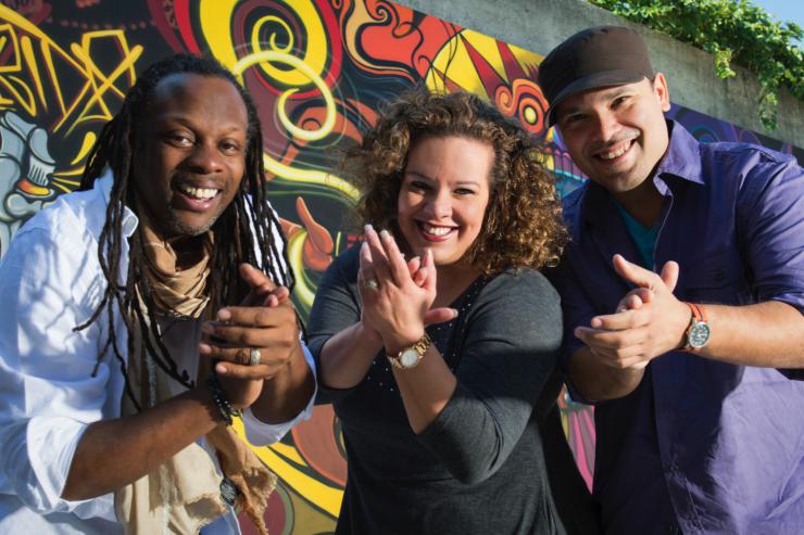 Three performers smiling in front of a mural.