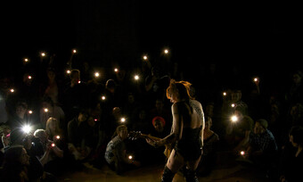 silhouette of performer playing guitar while audience watches, holding flashlights