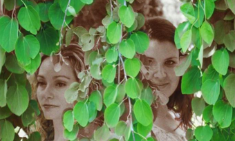 Two women standing among vines.