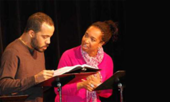 Two Black performers reading scripts on-stage.