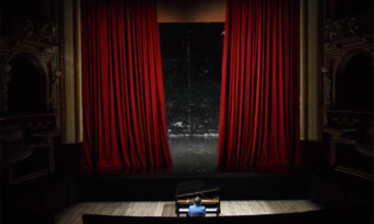 A man sits at a piano in front of a stage.