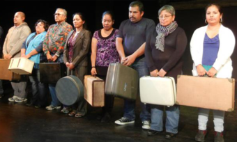 Eight performers in Ladybird stand on stage in a line and hold suitcases.