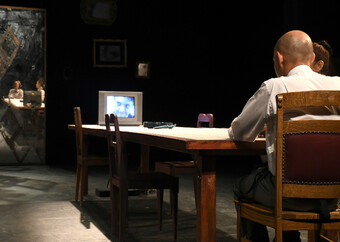 Actor staring at a television screen from across a table.