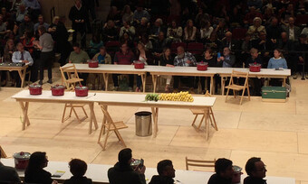 two audiences looking on a stage at two tables with food and pots on them