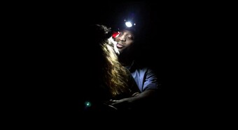 Two actors embrace, illuminated by a headlamp.