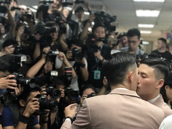 two men kissing in front of reporters with cameras