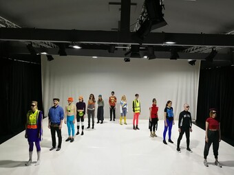several performers standing in a "V" formation dressed in colorful techno dance clothes.