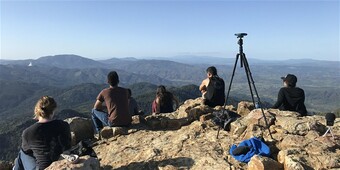 people sitting on a mountain facing away from camera with tripod in foreground