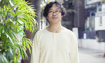 headshot of Toshiki Okada next to a plant