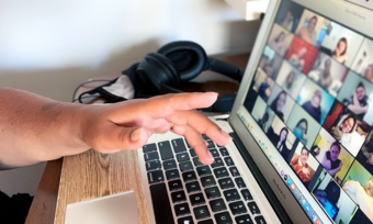 a hand reaching toward a laptop open to a zoom video call