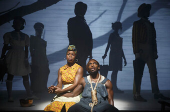 two actors onstage with five actors' shadows behind them