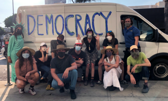 a group posing for a photo in front of a white van with "democracy" written on it