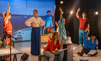 actors scattered across stage wearing red and blue clothing in performance.