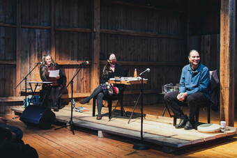 artists sitting on a wooden stage in front of microphones.