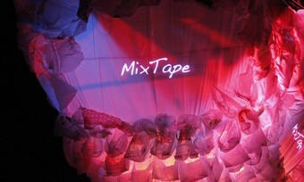 A floating jellyfish-like figure made out of a large sheet and plastic bags. The lighting is pink with the word mixtape on the sheet.