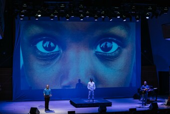 Three men on stage in front of a projection of someone's eyes.