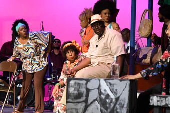 Seven Black actors performing on stage accompanied by the band.