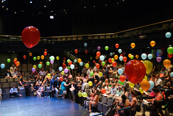 A picture of a theatre full of people holding balloons in the air.